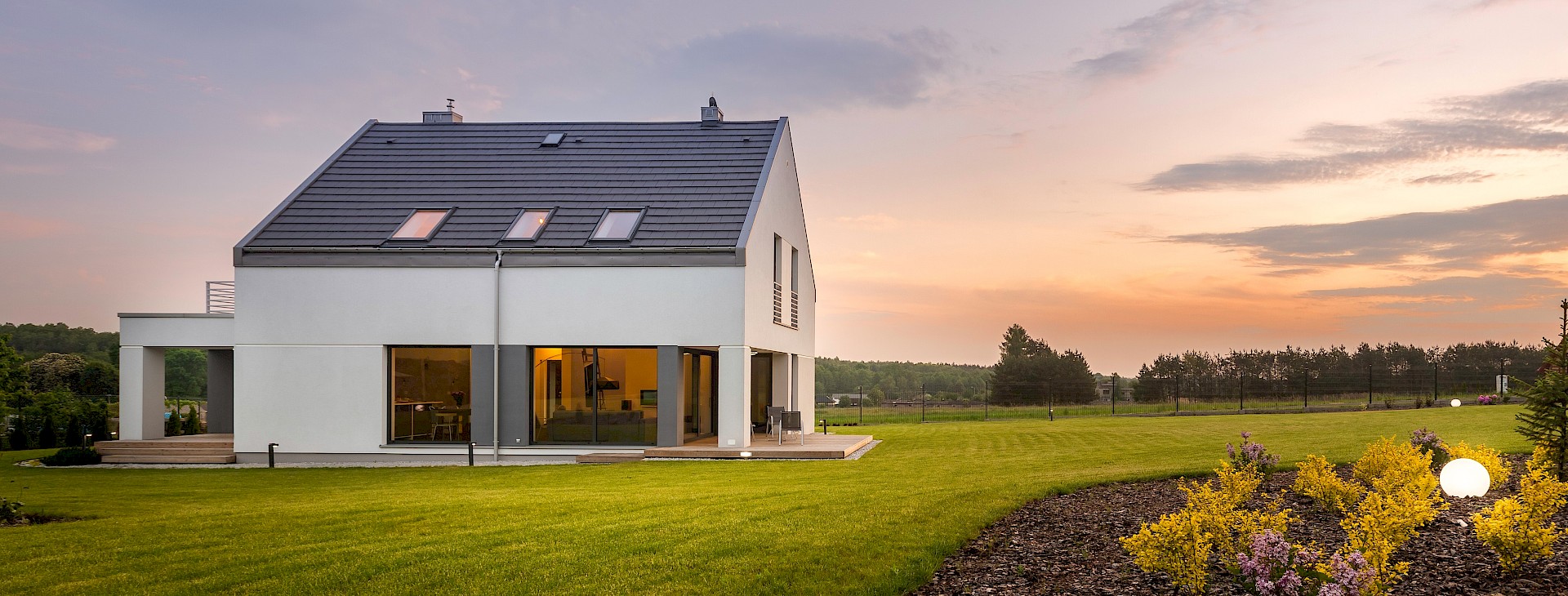 Modernes Haus mit Garten bei Sonnenuntergang.