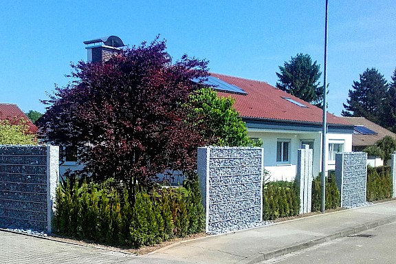 Haus mit modernem Sichtschutzzaun und Bäumen im Garten.